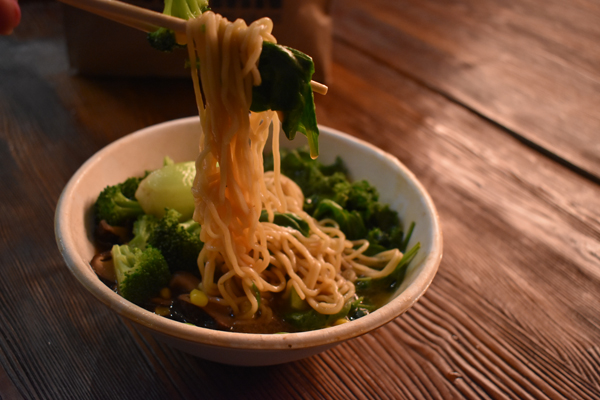 A bowl of warm ramen noodle soup with corn, bok choi and kale soaking up the pork broth.
