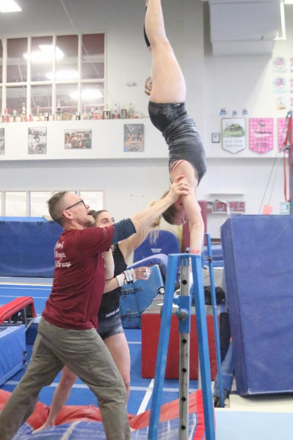 sophmore Katie Viles and Coach Byrnes spot Savannah Tafolla while she works on a handstand with the practice bar.