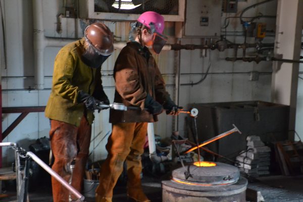 Sculpture Professor Brighton McCormick assists student Tavia Snyder in taking the temperature of molten bronze, which melts at around 1,700 degrees  Fahrenheit, as they prepare for another
round of filling molds.