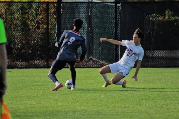 First-year defender Wylie Wright attempts a slide tackle on a Macalester player for control of the ball.