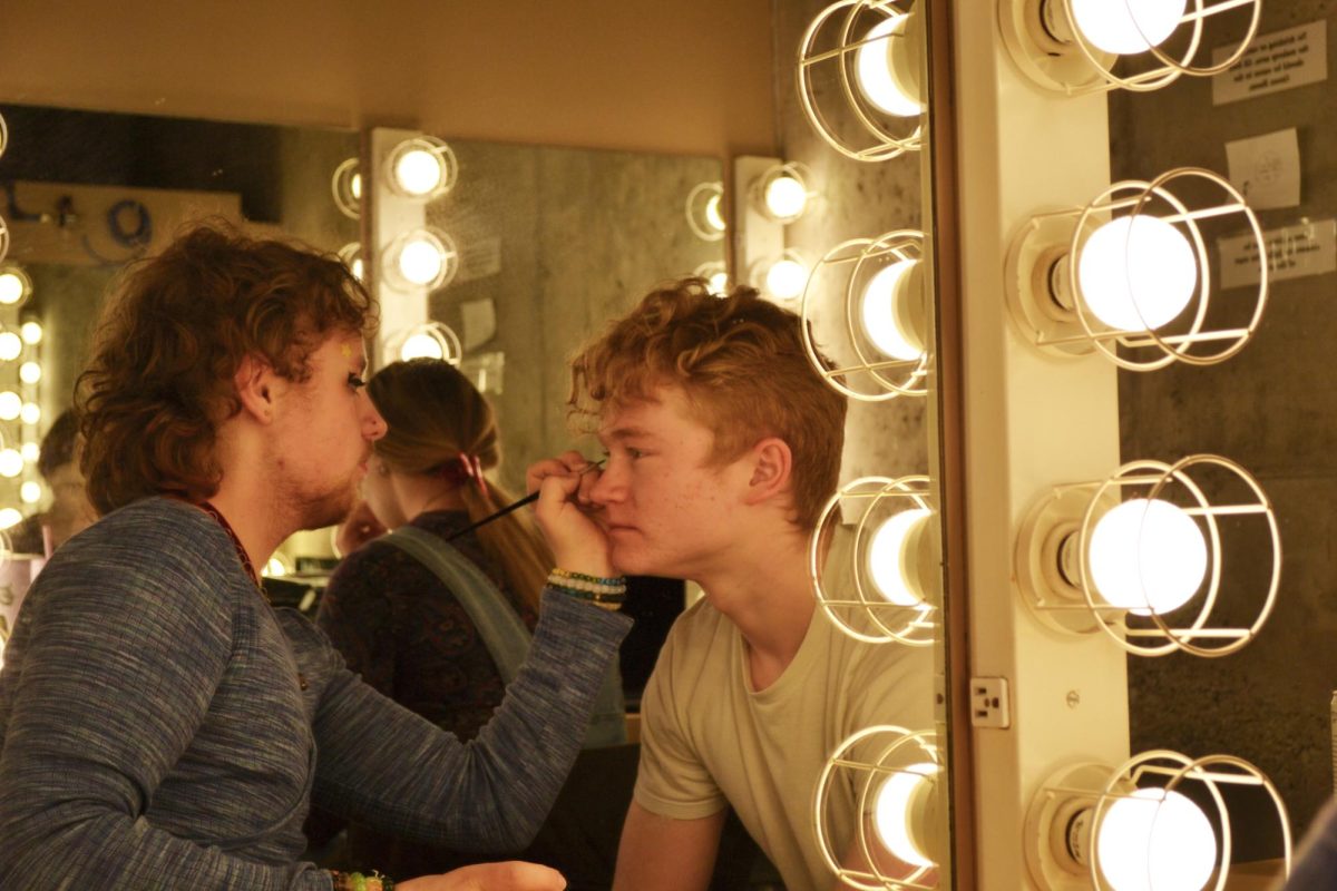 First-year Makeup Designer Liam Schrom (left) applies eye makeup for an uncanny-valley look for the character Cothurnus, played by sophomore Asher Gettings (right).