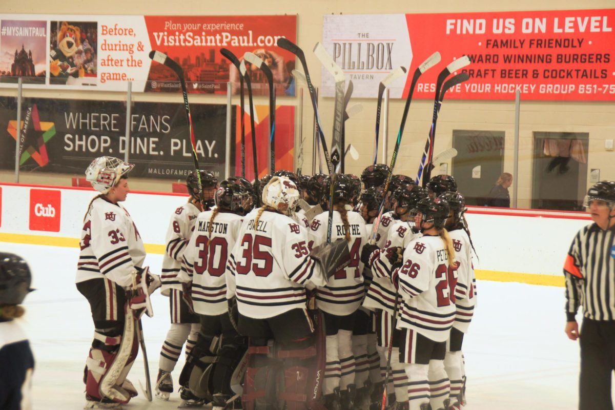 The Hamline Pipers celebrate their 1-0 victory over the Bethel Royals, huddling together and raising their hockey sticks in the air triumphantly.
