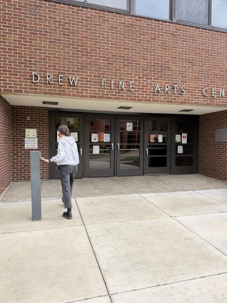 A student uses the accessible entrance button to enter the Drew Fine Arts Center at the one accessible entrance for the building.