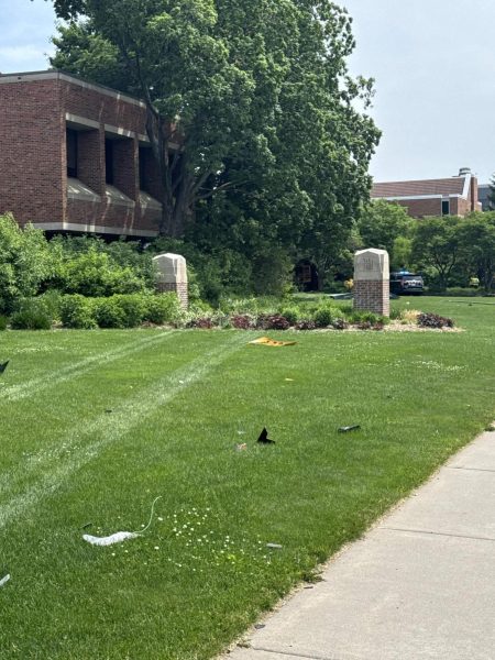A bus' tire tracks lead through the grass of Hamline University, through a destroyed sign.